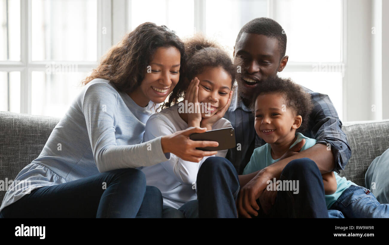 Sorridente famiglia nero rilassarsi insieme guardare cartoni sullo smartphone Foto Stock