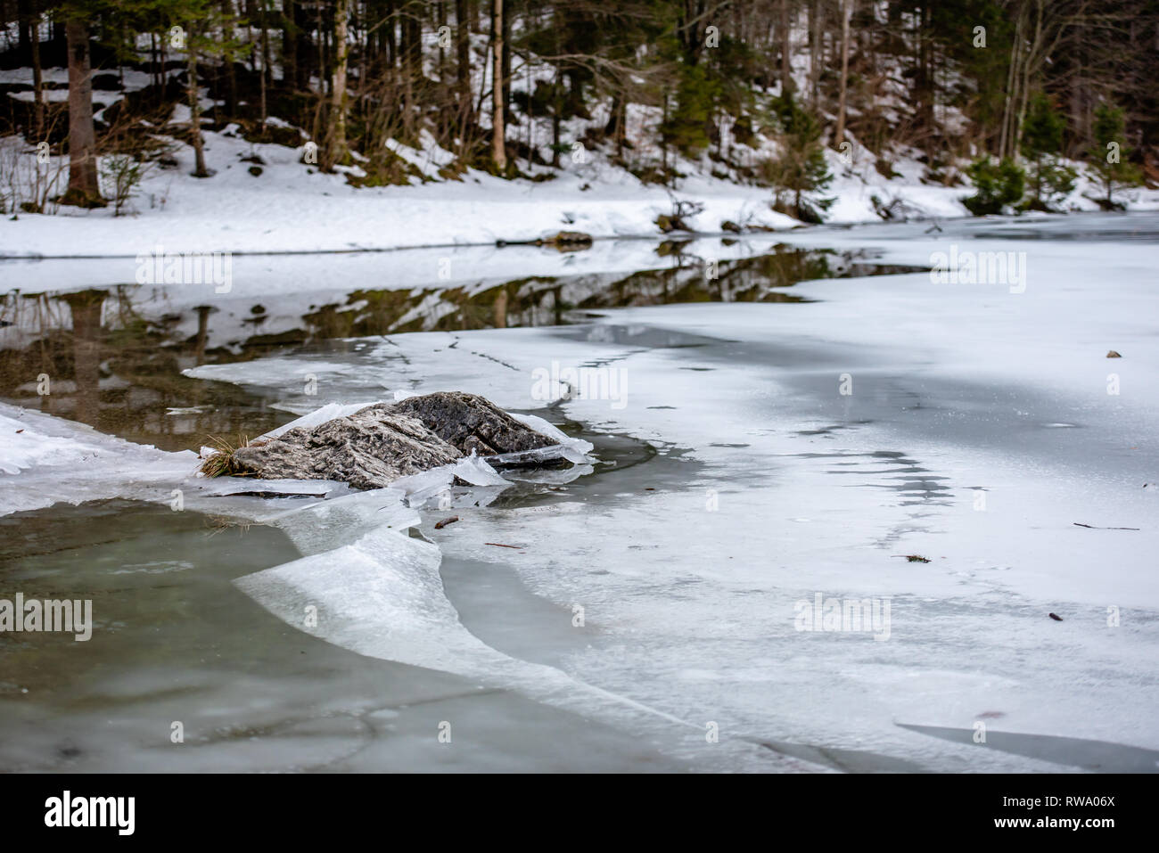 Uno spesso strato di ghiaccio sul lago ghiacciato a Vorderer Langbathsee. Belle montagne dalle vette innevate riflessa nelle acque cristalline del lago Foto Stock