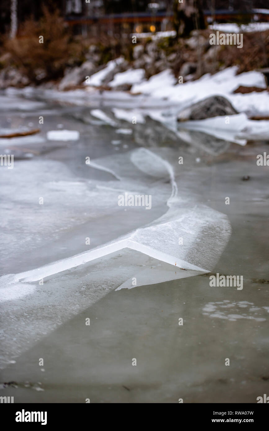Uno spesso strato di ghiaccio sul lago ghiacciato a Vorderer Langbathsee. Belle montagne dalle vette innevate riflessa nelle acque cristalline del lago Foto Stock