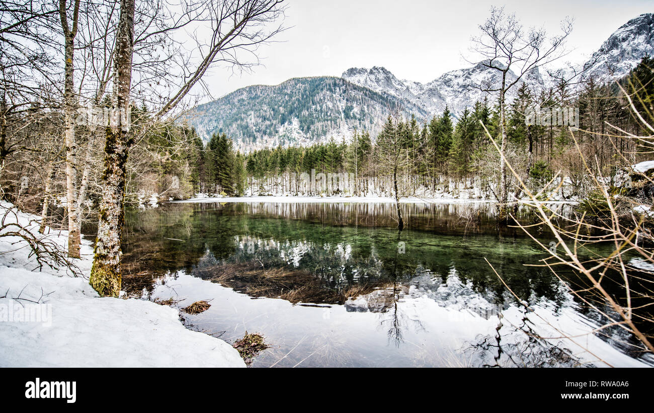 Uno spesso strato di ghiaccio sul lago ghiacciato a Vorderer Langbathsee. Belle montagne dalle vette innevate riflessa nelle acque cristalline del lago Foto Stock