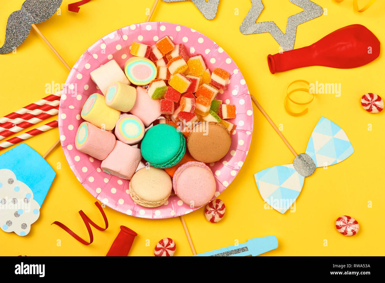 Parte colorata, caramelle e coriandoli su sfondo giallo top view mockup Foto Stock
