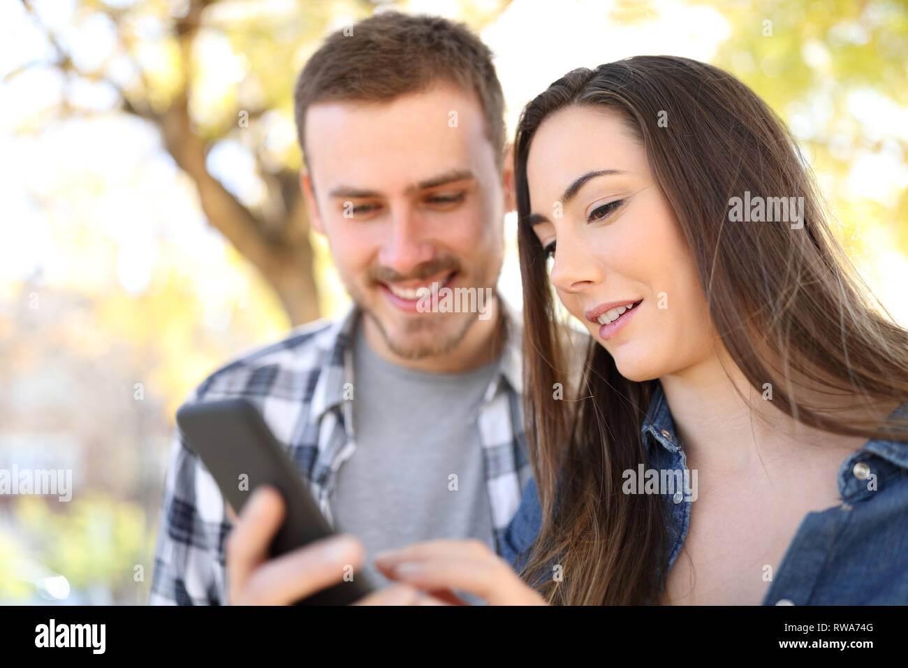 Felice coppia utilizzando smart phone controllando il contenuto online di un parco Foto Stock