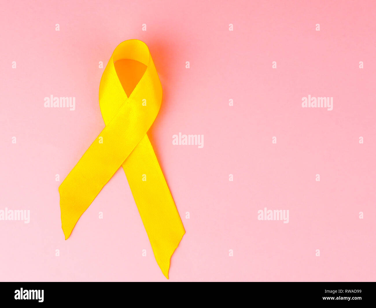 Cancro infantile consapevolezza nastro giallo su sfondo rosa. Cancro durante l'infanzia giornata. Foto Stock