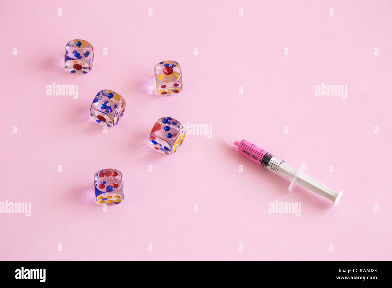 Dadi di gioco e la siringa contro di rosa pastello minima di sfondo abuso di sostanze stupefacenti e gioco d'azzardo concetto creativo. Foto Stock
