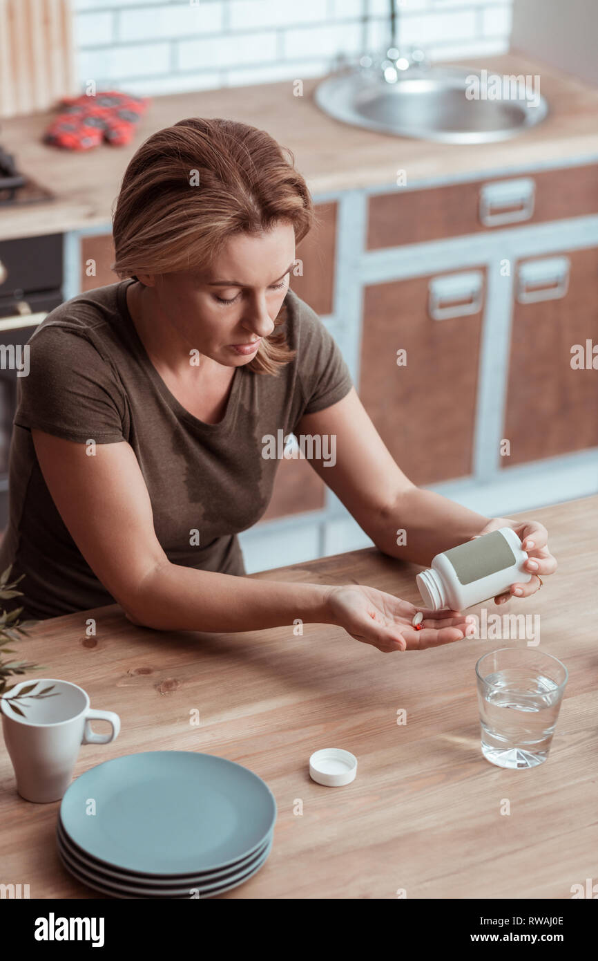 Malati e stanchi donna prendendo antidepressivo pillole in cucina Foto Stock