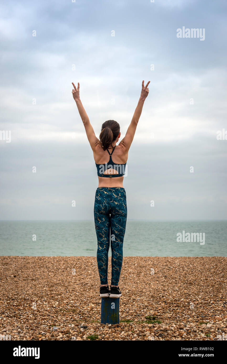 Donna in piedi con le braccia sollevate sulla spiaggia, vista posteriore, copyspace Foto Stock