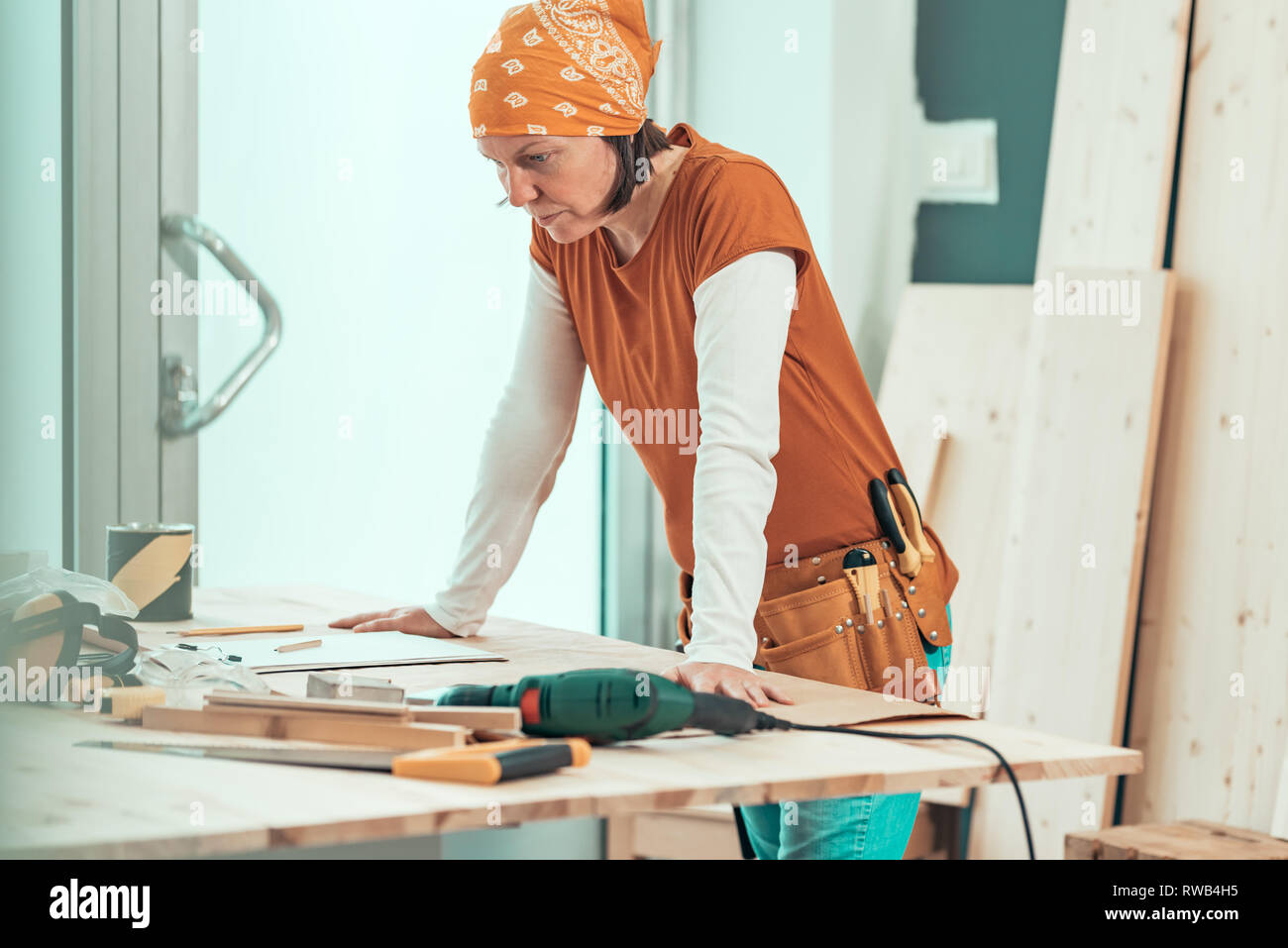 Falegname femmina con bandana in posa di laboratorio di falegnameria, piccoli imprenditori al luogo di lavoro Foto Stock