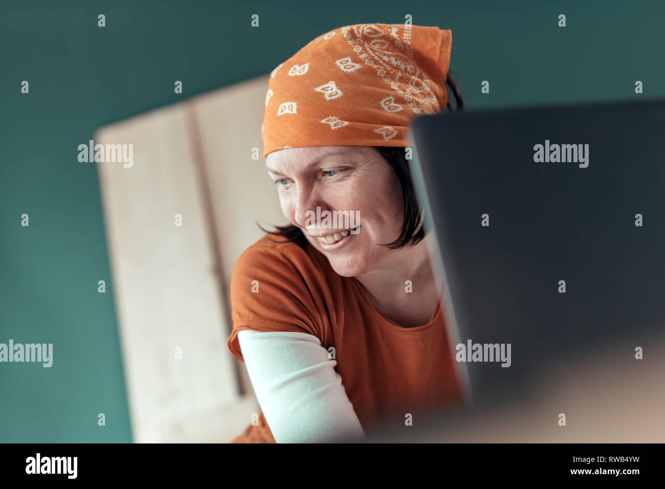 Sorridenti falegname femmina durante la chat online con il client sul computer portatile nel laboratorio di falegnameria Foto Stock