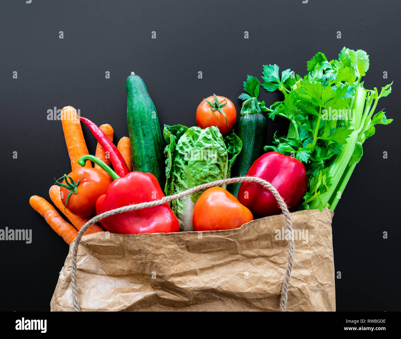 Fresche verdure organiche in carta marrone sacchetto contro scuro dello sfondo della tabella Foto Stock