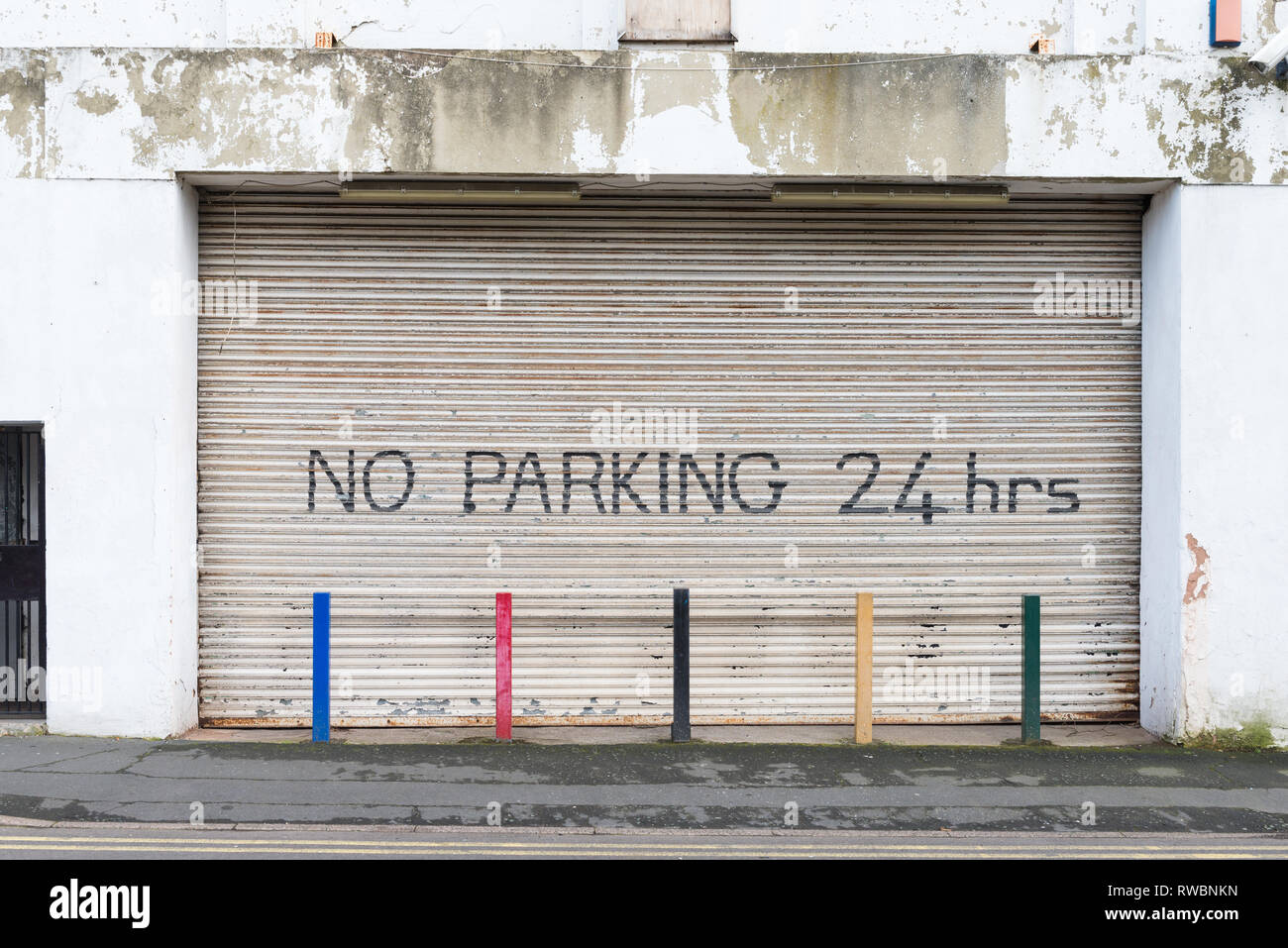 Grande rullo industriale otturatore chiuso con la scrittura di alcun parcheggio 24 ore e colonnine colorate Foto Stock
