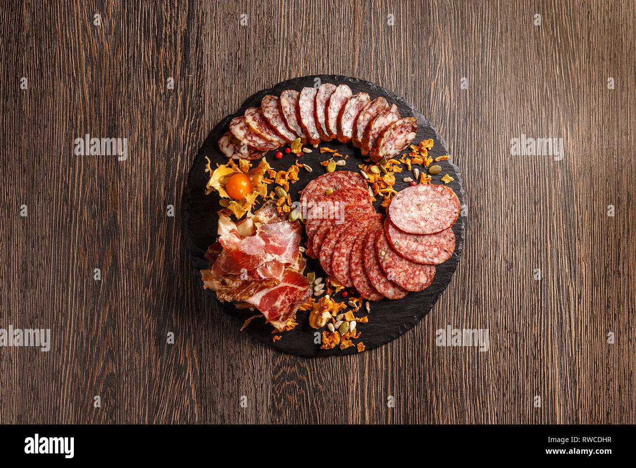 Spuntini da una varietà di affettati, pancetta, salsicce sono serviti su una scheda di ardesia su uno sfondo di legno. Vista da sopra. Lay piatto. Foto Stock