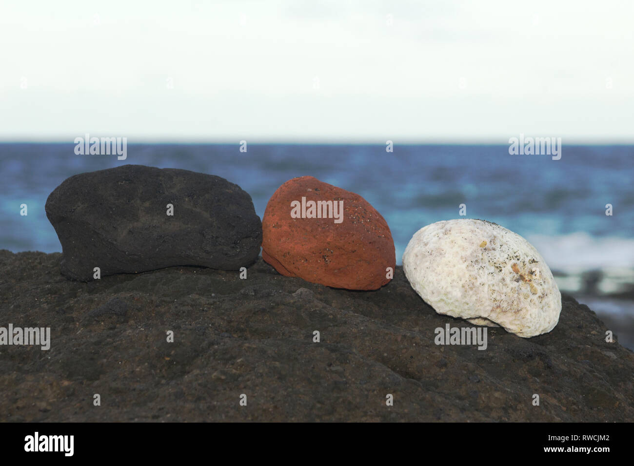 Una roccia vulcanica nera, un rosso ocra rock e un pezzo di corallo bianco contrasto contro ogni altro e il black rock si siedono su in spiaggia Foto Stock