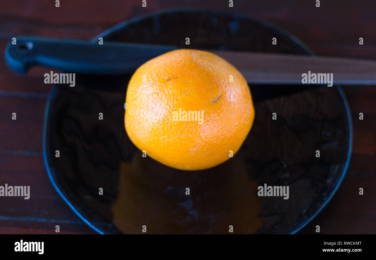 Un arancione su un piatto pronto a tagliare con un coltello. Foto Stock