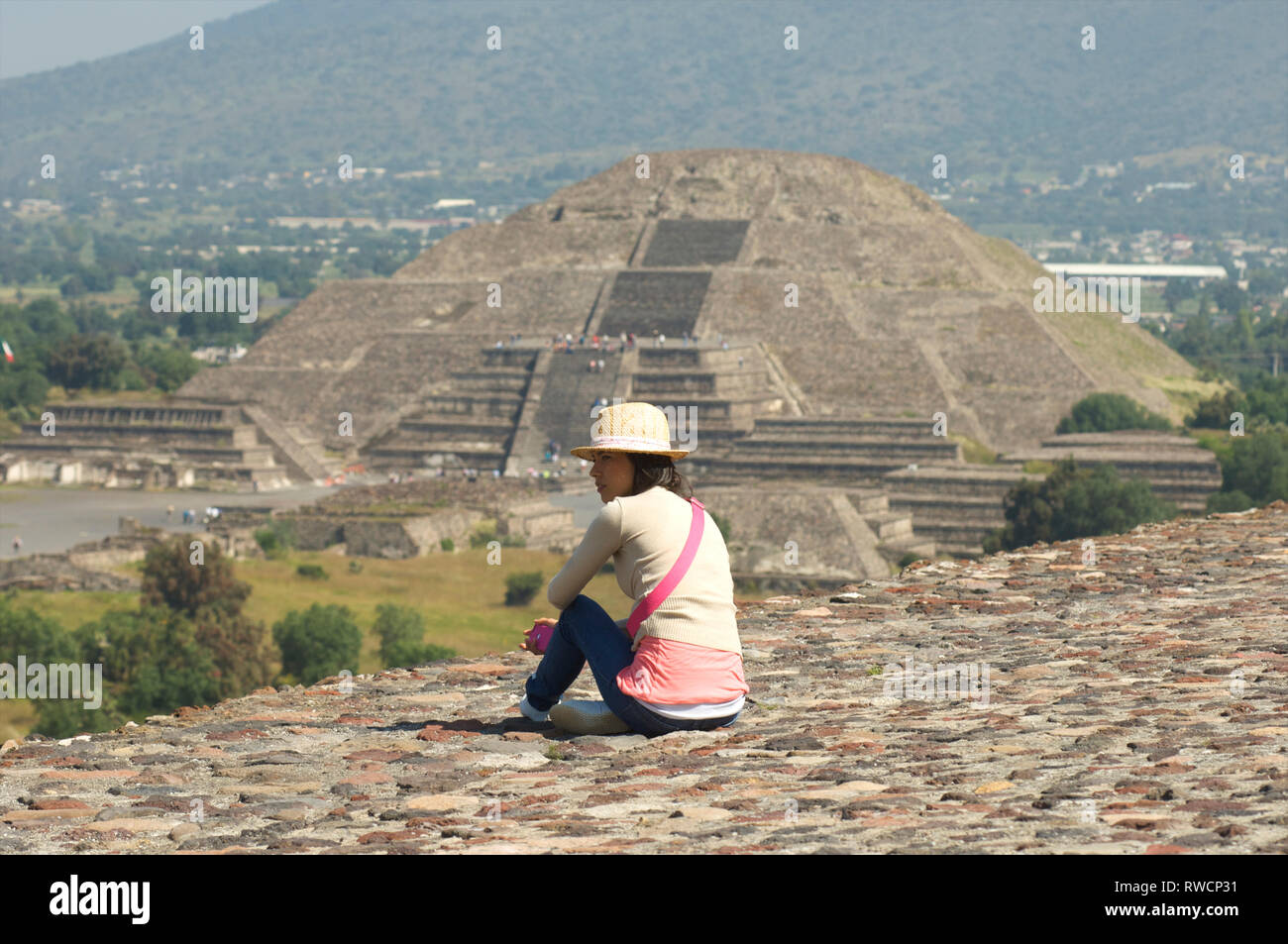 Donna seduta sulla sommità della Piramide del sole con la Piramide della Luna in background a Teotihuacan, Messico Foto Stock