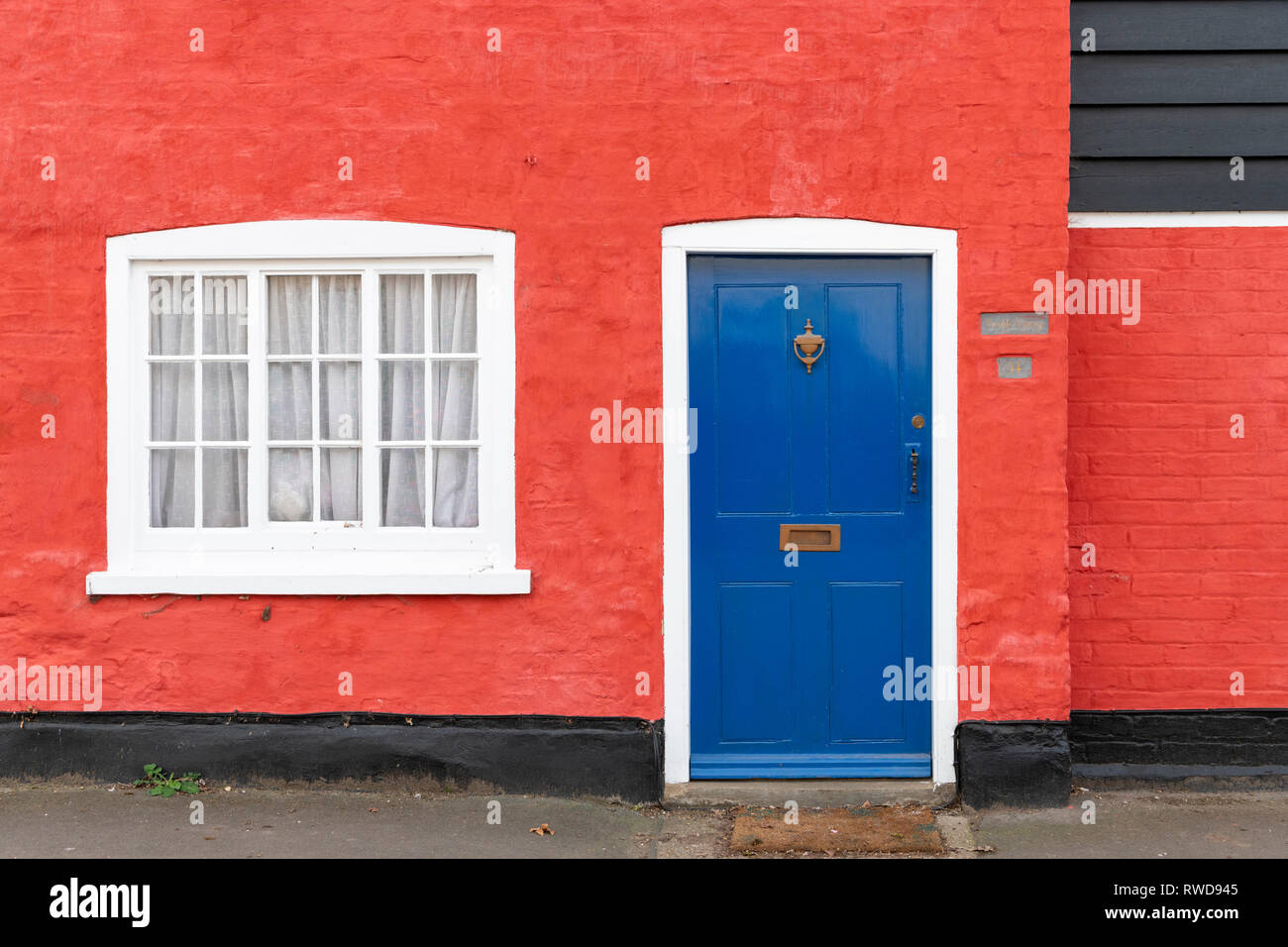 Un vivacemente colorato cottage in un villaggio del Regno Unito con pareti rosse e blu di una porta. Foto Stock