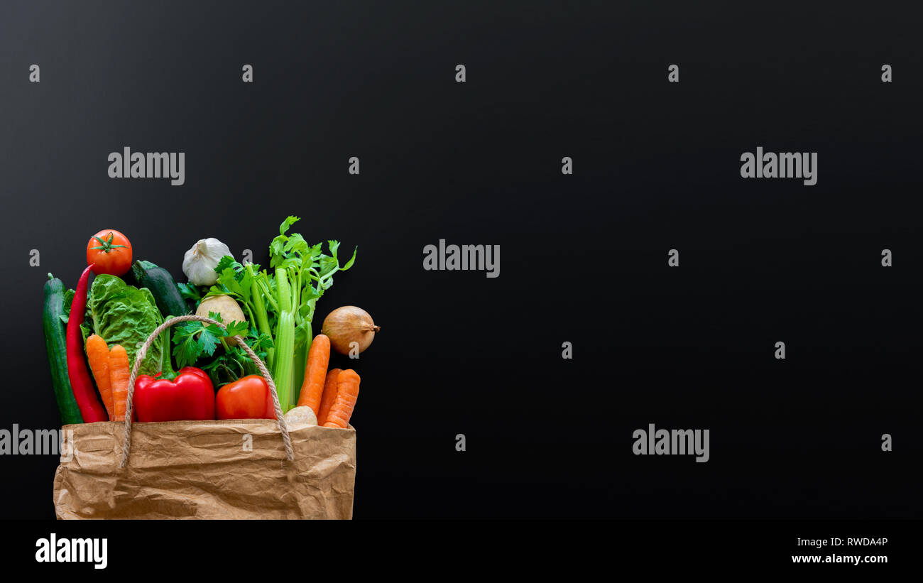 Fresche verdure organiche in carta marrone sacchetto contro scuro dello sfondo della tabella Foto Stock