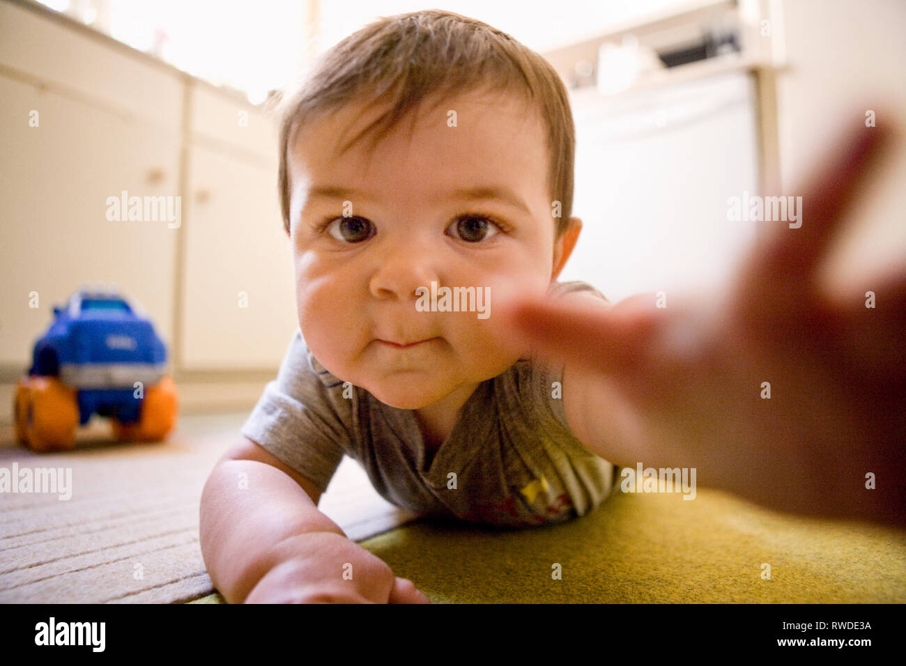Bambino giacente su un piano raggiunge per la fotocamera. Foto Stock