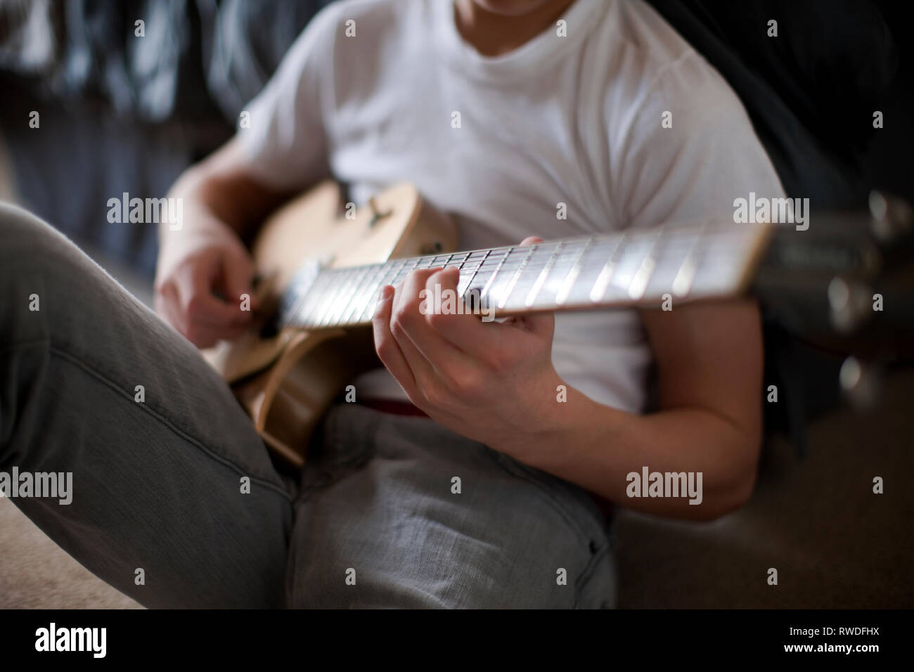 Ragazzo seduto sul letto a suonare la chitarra. Foto Stock