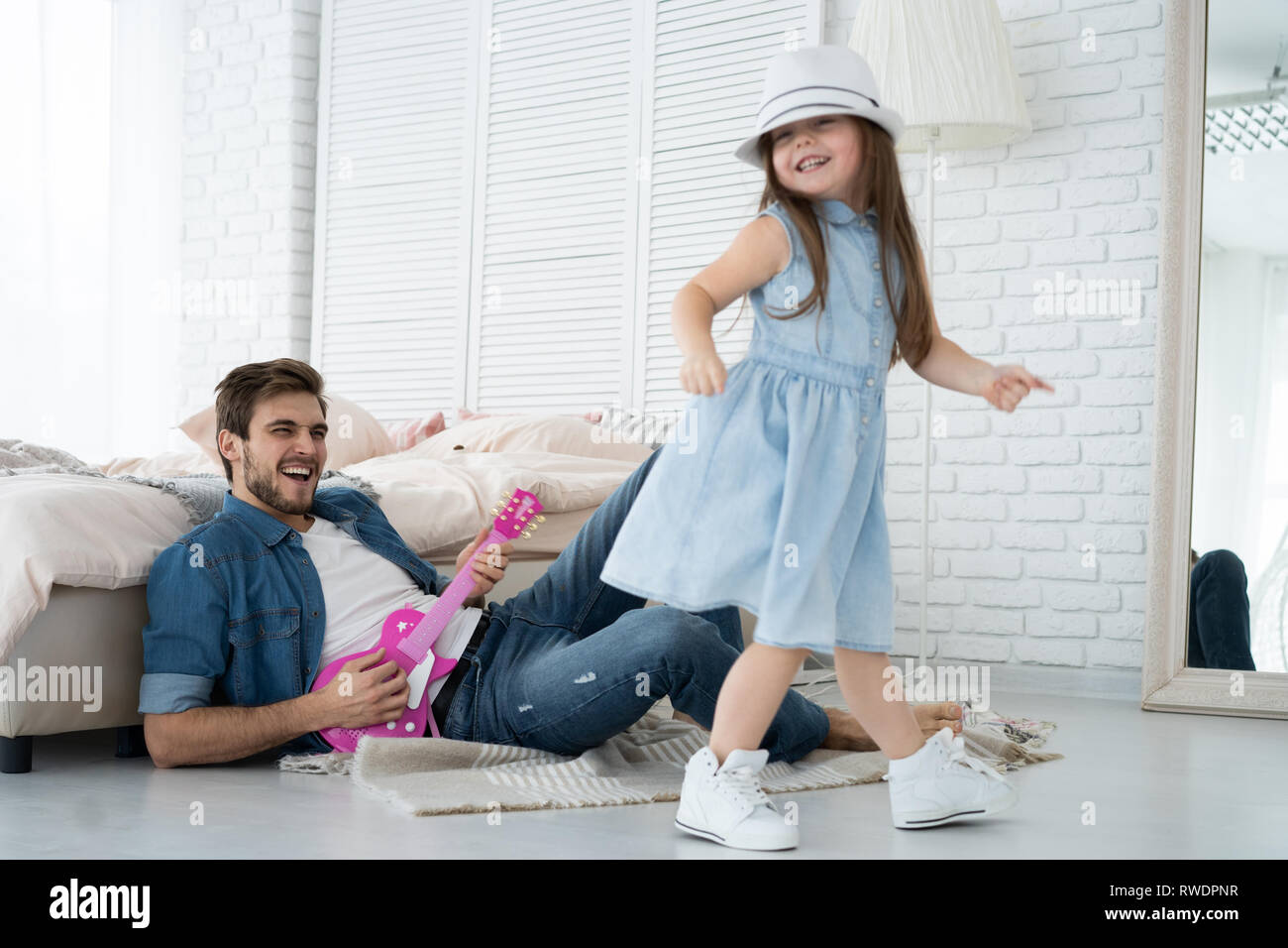 Divertirsi insieme. Giovane padre suonare la chitarra per la sua piccola figlia e sorridenti mentre spendere tempo libero a casa. Foto Stock