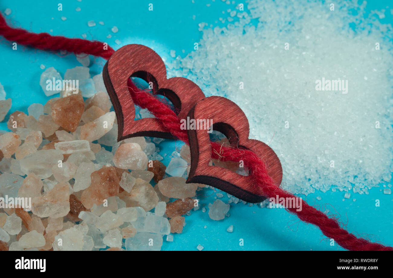 Due decorativi in legno cuori filettato su corda rossa con un mucchio di grezzo dei cristalli di sale su di un lato e tritato fine sale o zucchero grani sull'altra in Foto Stock