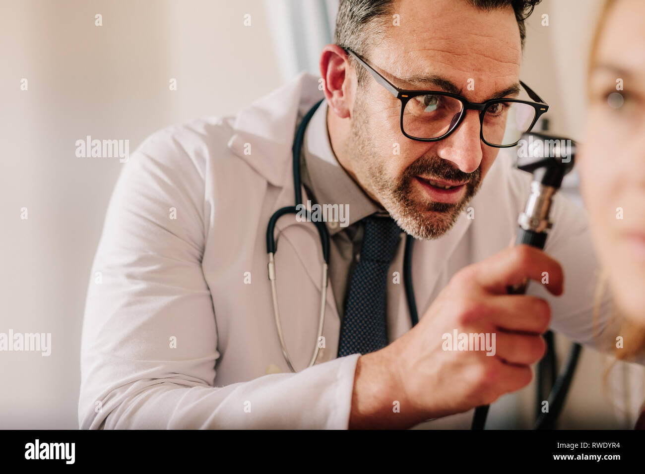 Esperto medico ORL cercando in orecchio del paziente con un otoscopio. Medico maschio esaminando orecchio del paziente con strumento a sua clinica. Foto Stock