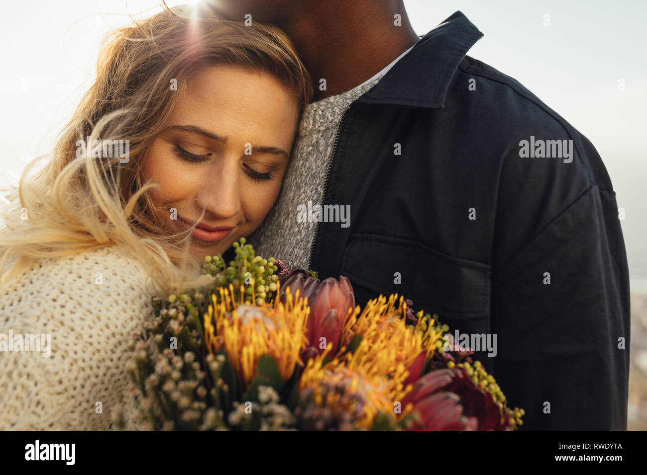 Giovane donna che abbraccia il suo fidanzato con fiori. Donna che abbraccia il suo uomo con amore. Foto Stock