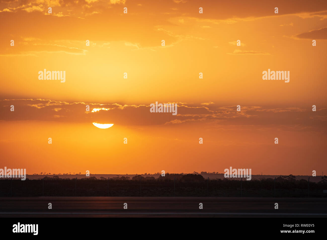 Il sole parzialmente dietro il cloud in un arancione tramonto su campi in Victoria Australia Foto Stock