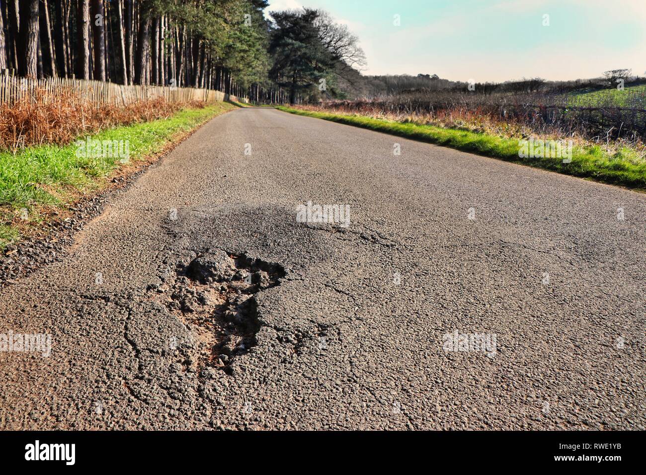 Una singola buca su un altrimenti vuota country road. Foto Stock