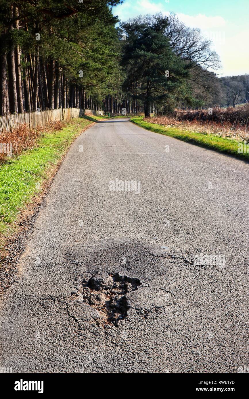 Una singola buca su un altrimenti vuota country road. Foto Stock