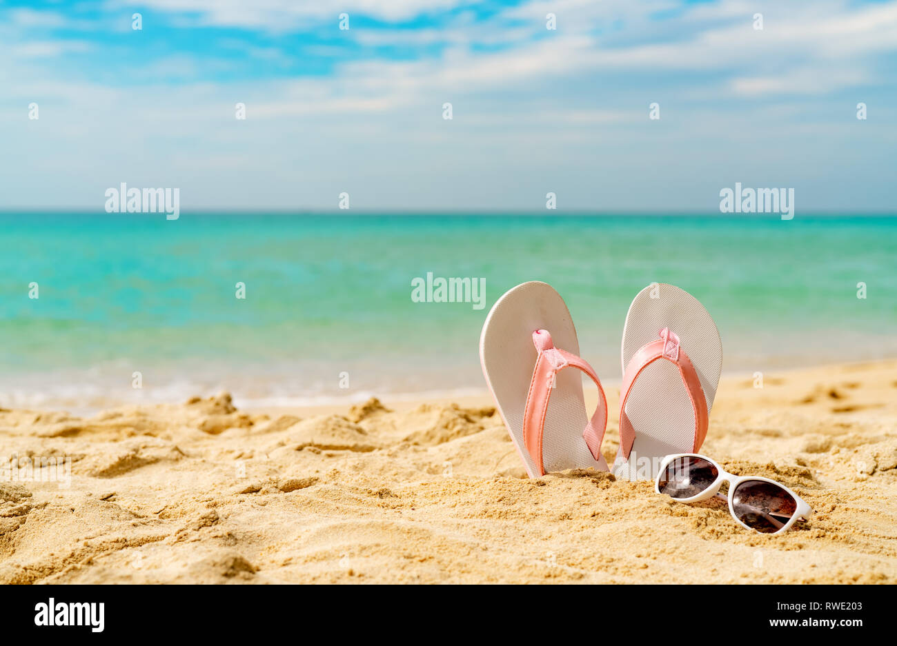 Rosa e Bianco sandali, occhiali da sole sulla spiaggia di sabbia in riva al mare a. Moda casual style flipflop e bicchieri. La vacanza estiva sulla spiaggia tropicale. Vacanza divertente Foto Stock
