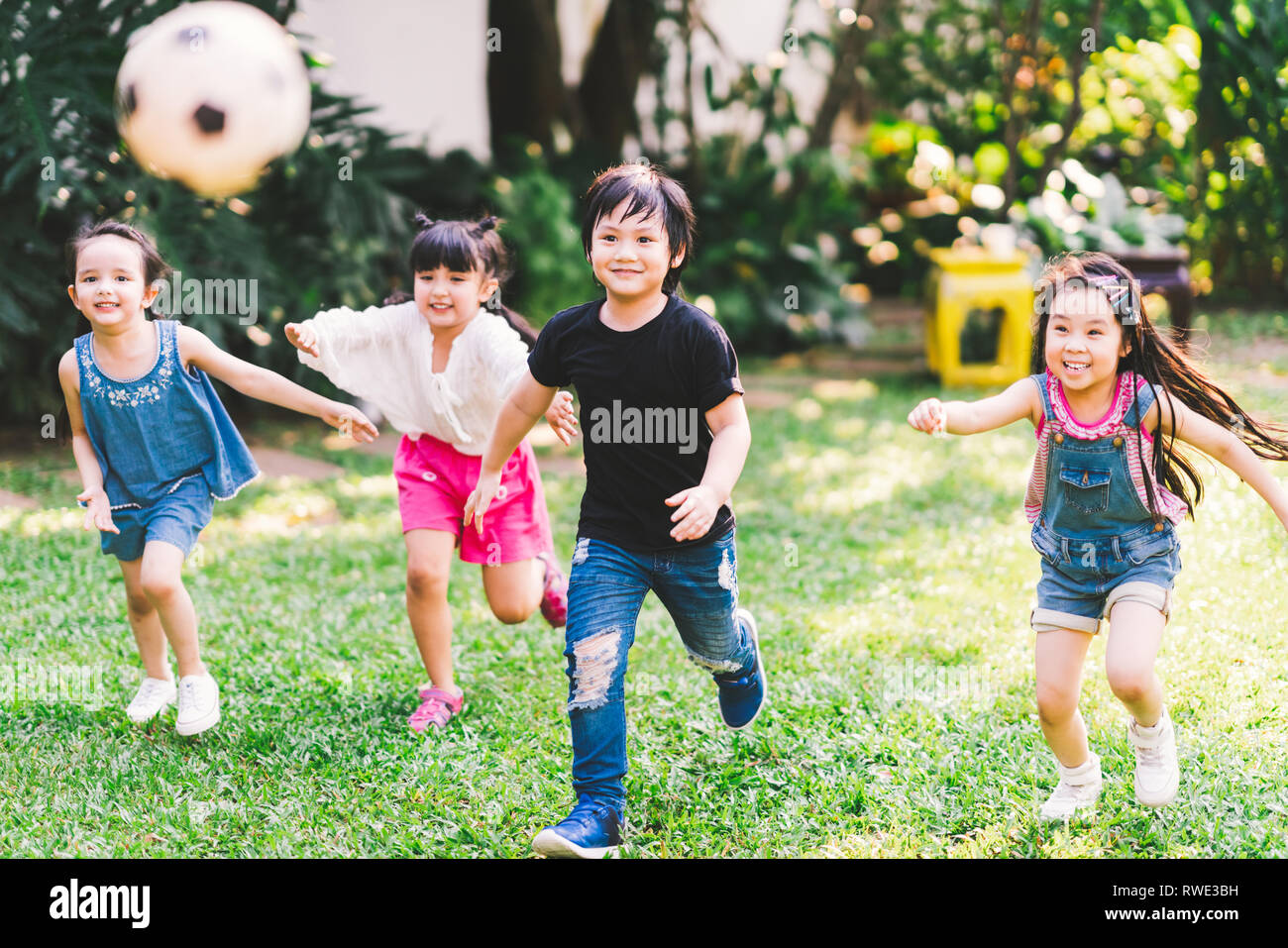 Asiatici e razza mista felice giovani bambini che correvano giocando a calcio insieme nel giardino. Multi-etnico gruppo di bambini, outdoor sport esercitare, gioco libero Foto Stock