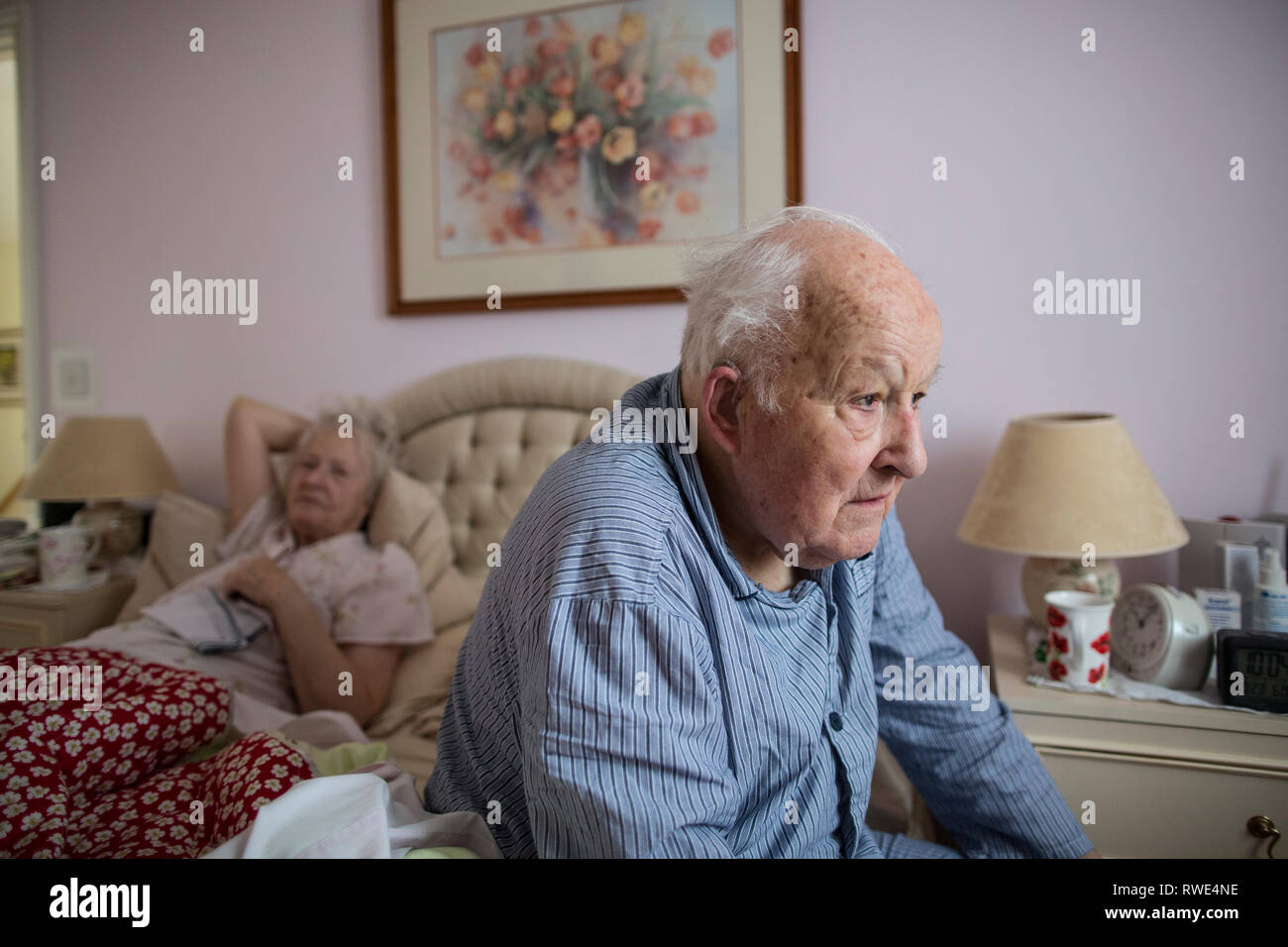 Coppia di anziani nel loro 80's nella loro camera da letto a casa indossando i loro pigiami a mattina tempo, England, Regno Unito Foto Stock