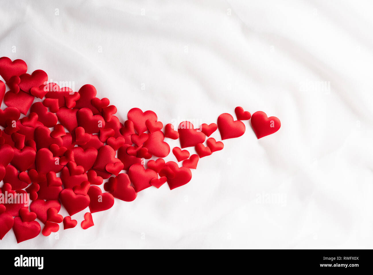 Il giorno di San Valentino e il simbolo dell'amore. Flying cuori rossi su tessuto bianco sullo sfondo. Foto Stock