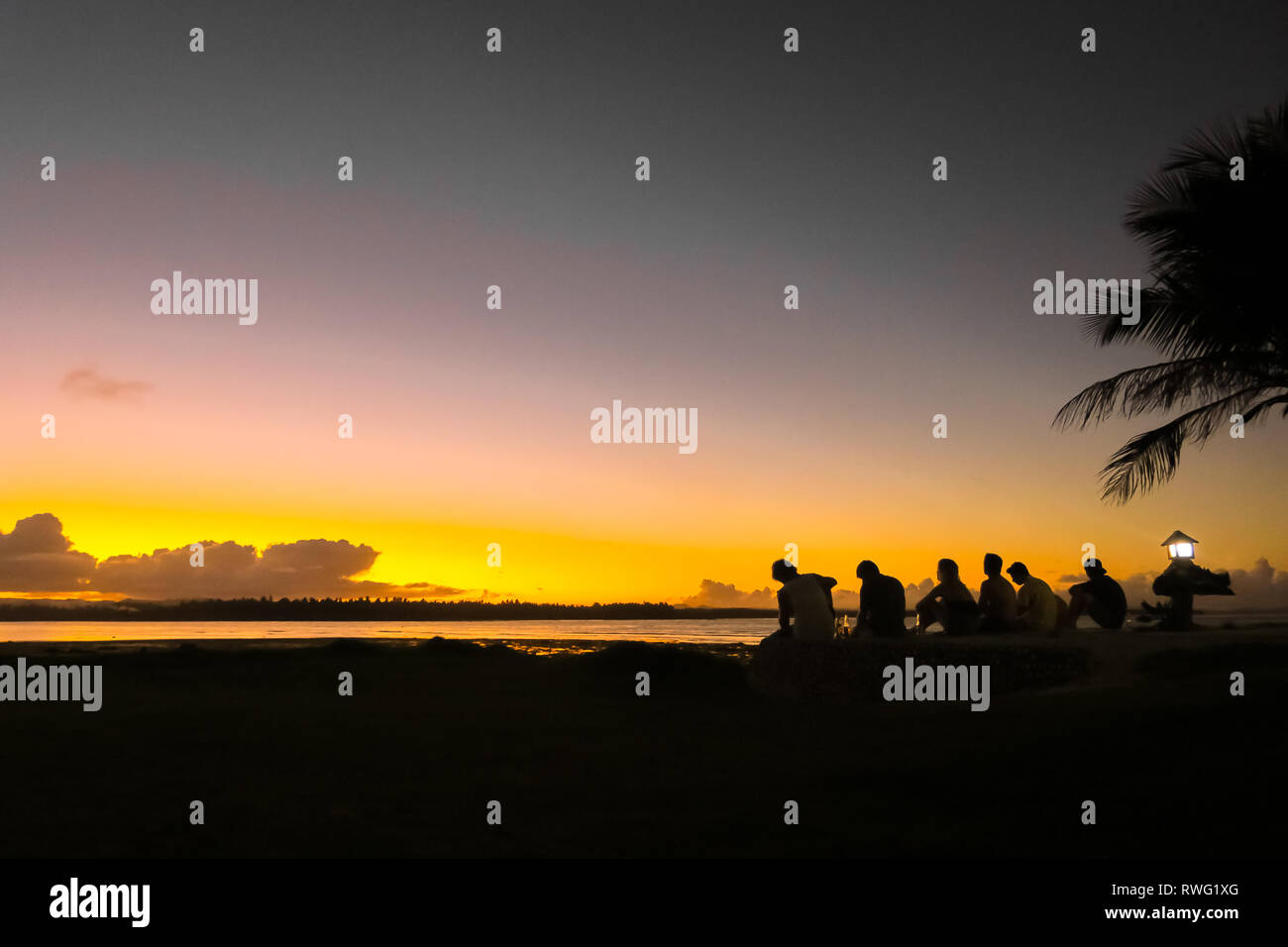 Gruppo di amici godendo di un bel colore arancione tramonto dell'isola, seduto sulla spiaggia - Cloud 9, Siargao - Filippine Foto Stock