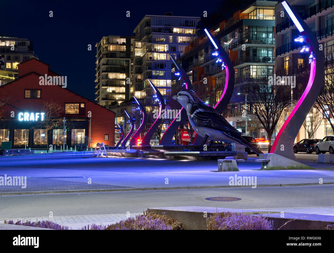 Olympic Village Square a Vancouver in Canada di notte, con una grande scultura di uccelli e birreria artigianale. Vancouver il Villaggio Olimpico di sviluppo. Foto Stock
