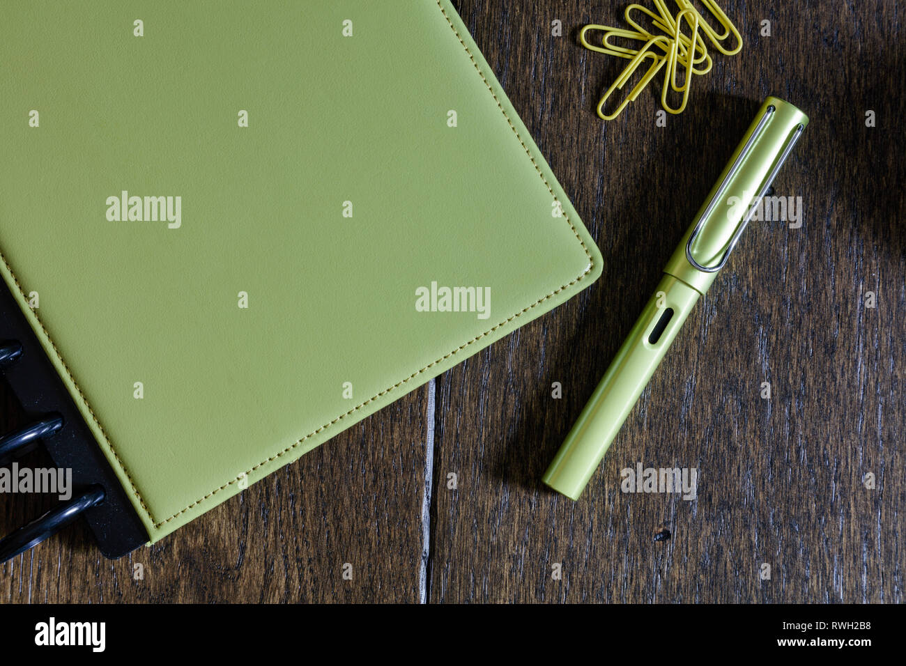 Vicino allo studio di una raccolta di articoli di cancelleria in verde lime - notebook, penna stilografica e graffette su vintage scrivania in legno Foto Stock