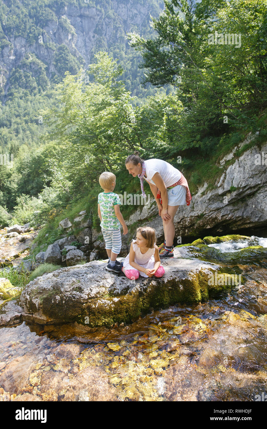 Madre con bambini divertirsi e giocare da un torrente di montagna in estate. Uno stile di vita naturale e positivo, parenting infanzia concetto di esperienza. Foto Stock