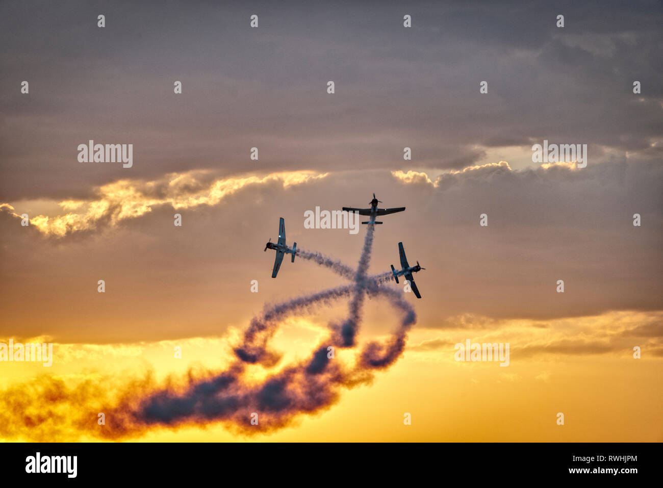 Tre aerei acrobatici attraversando nel cielo contro le nuvole e un cielo arancione Foto Stock