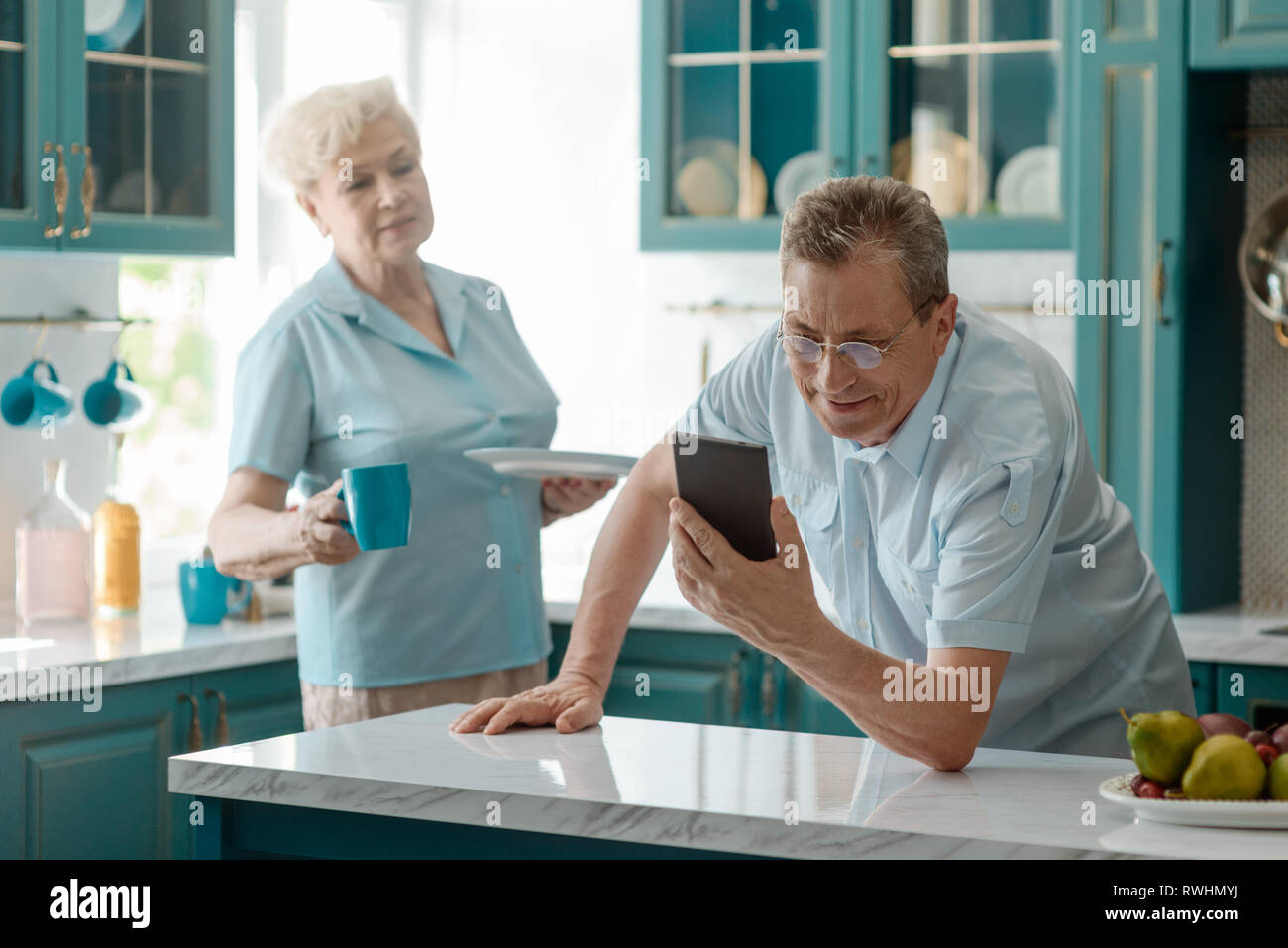 Uomo in pensione, addicted allo smartphone, la lettura di notizie, mentre sua moglie arrabbiato portò una tazza di tè. Dipendenza da digitale a rovinare la vita. Foto Stock