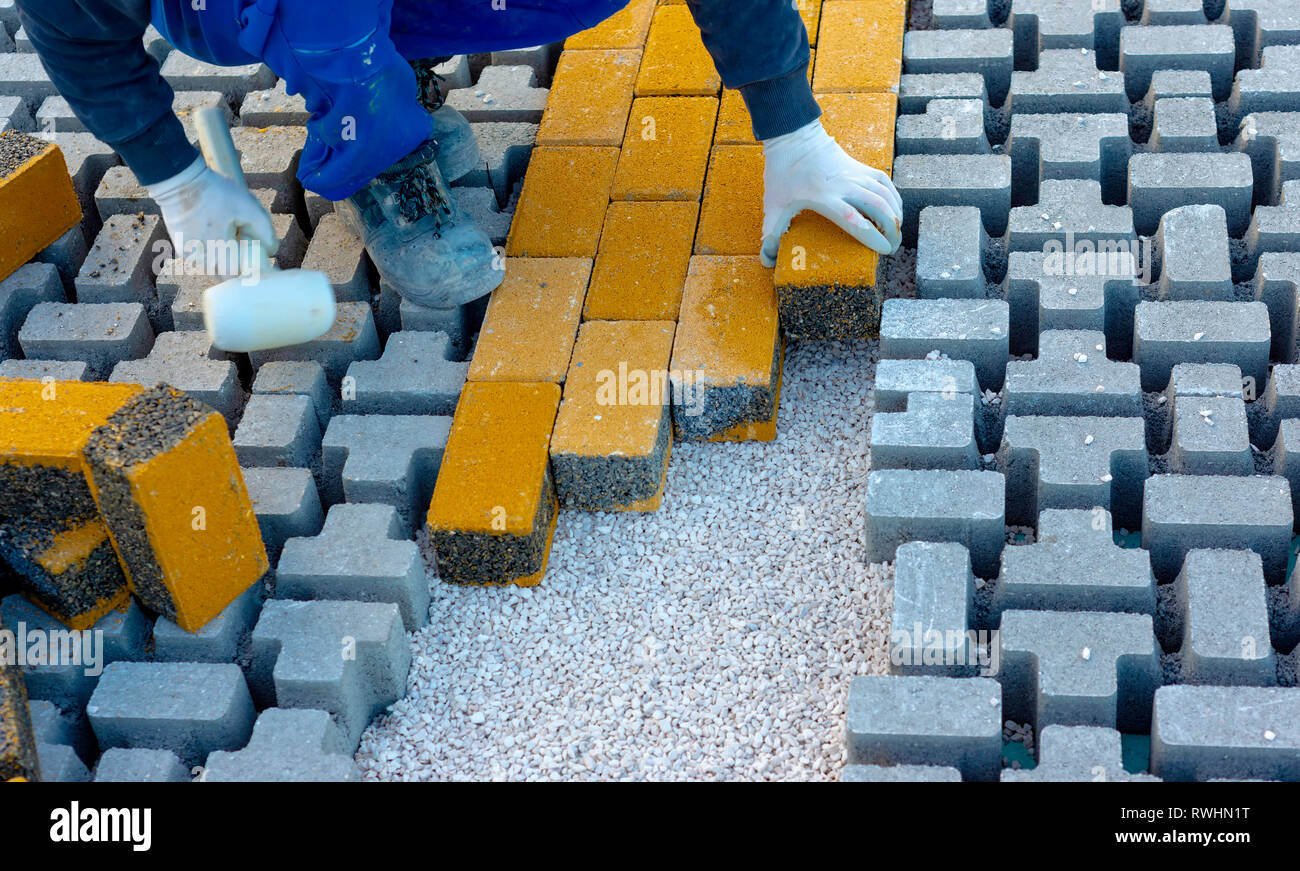 Pavimentazione in pietra lavoratore è mettere giù lastricatori durante la costruzione di una strada di città sul foglio non tessuto sabbia di biancheria da letto e di un loro montaggio in posizione. Foto Stock