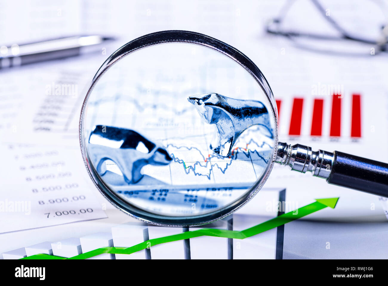 Toro e orso con tabelle, grafici e una lente di ingrandimento Foto Stock