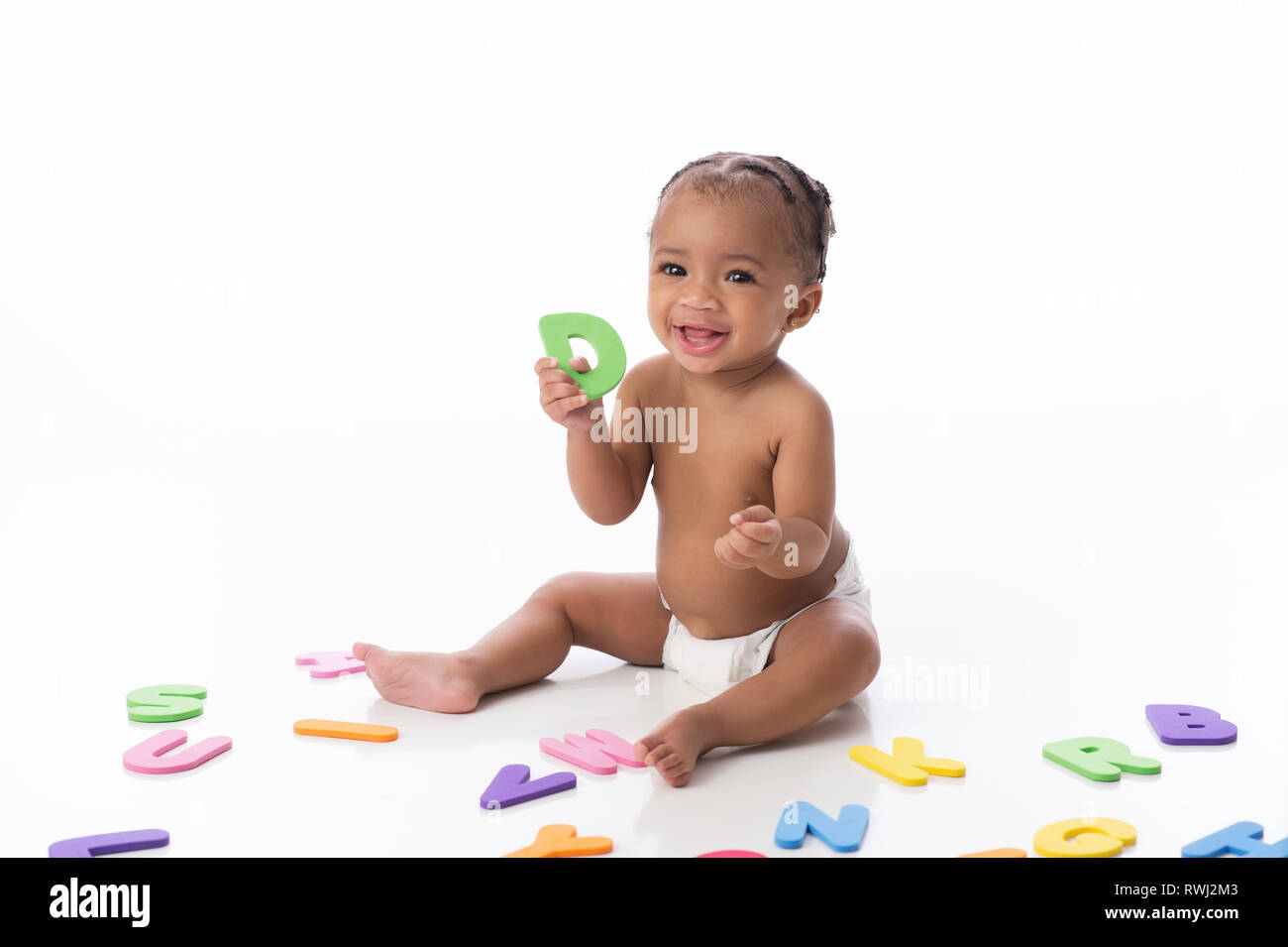 Un sorridente sei mesi bambina indossa un pannolino bianco. Lei è seduta su un bianco sfondo senza giunture e giocare con alfabeto di schiuma giocattoli. Foto Stock