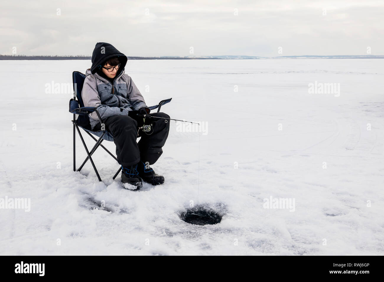 Ragazzo aspettando pazientemente per un morso mentre la pesca sul ghiaccio al lago Wabamun; Wabamun, Alberta, Canada Foto Stock