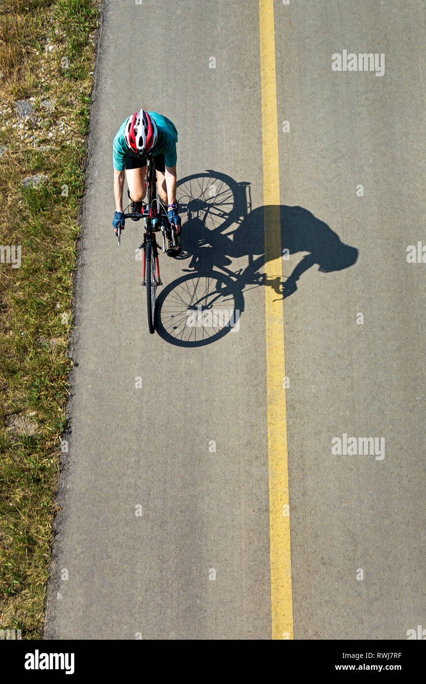 Vista aerea guardando in giù su un ciclista femmina su un sentiero pavimentato con ombra del ciclista; Calgary, Alberta, Canada Foto Stock