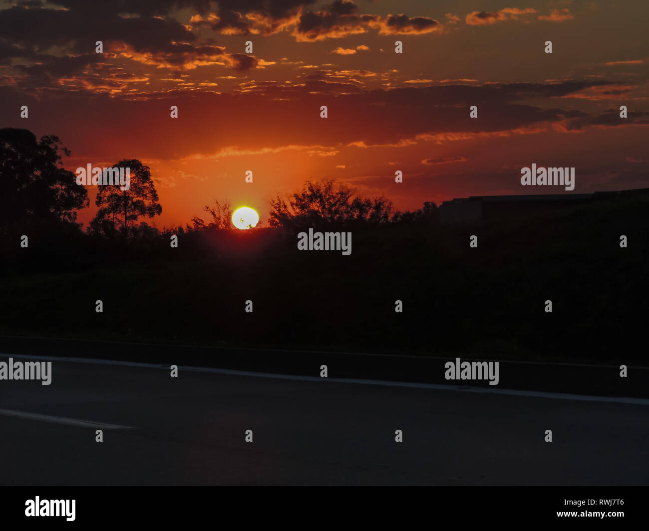 Una bella vista di un tramonto rossastro con una strada scura in primo piano e sfondo nero Foto Stock