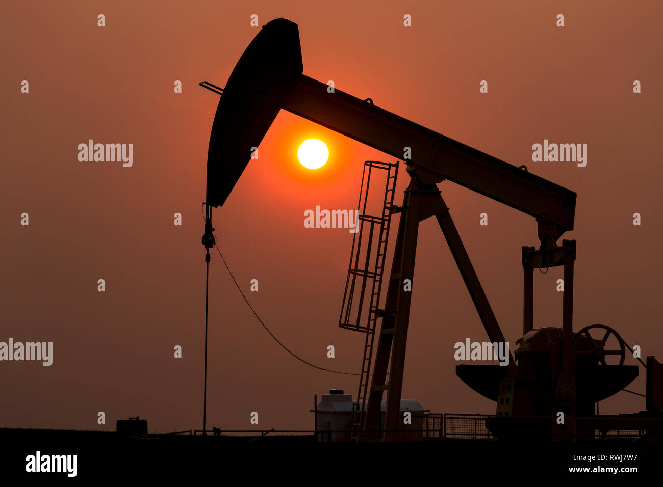 Silhouette di pumpjack con un incandescente caldo sole palla in background, a ovest di Airdrie; Alberta, Canada Foto Stock