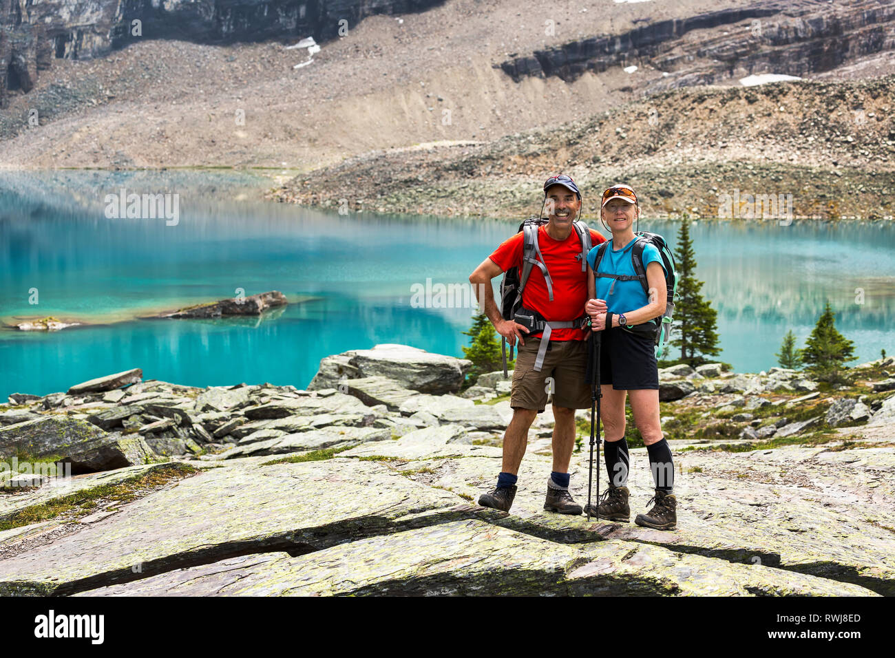 Maschi e femmine di escursionista in piedi in una grande zona rocciosa con colorati lago alpino e scogliere di montagna in background; British Columbia, Canada Foto Stock