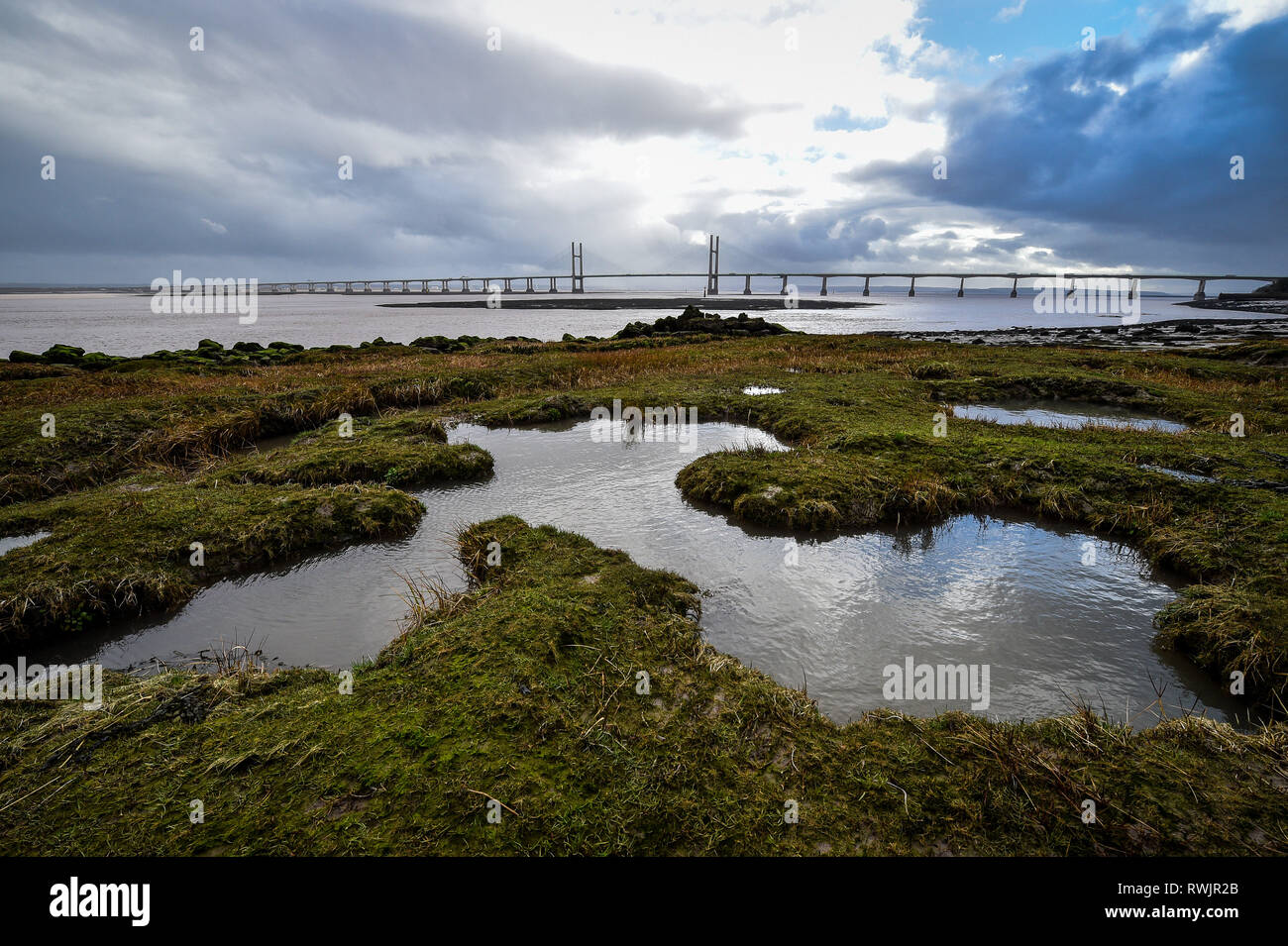 Pozze di acqua di mare forma on Grassy banche che sono esposti durante la bassa marea in Severn Estuary sotto il cielo tempestoso come heavy rain scende oltre il canale di Bristol. Foto Stock