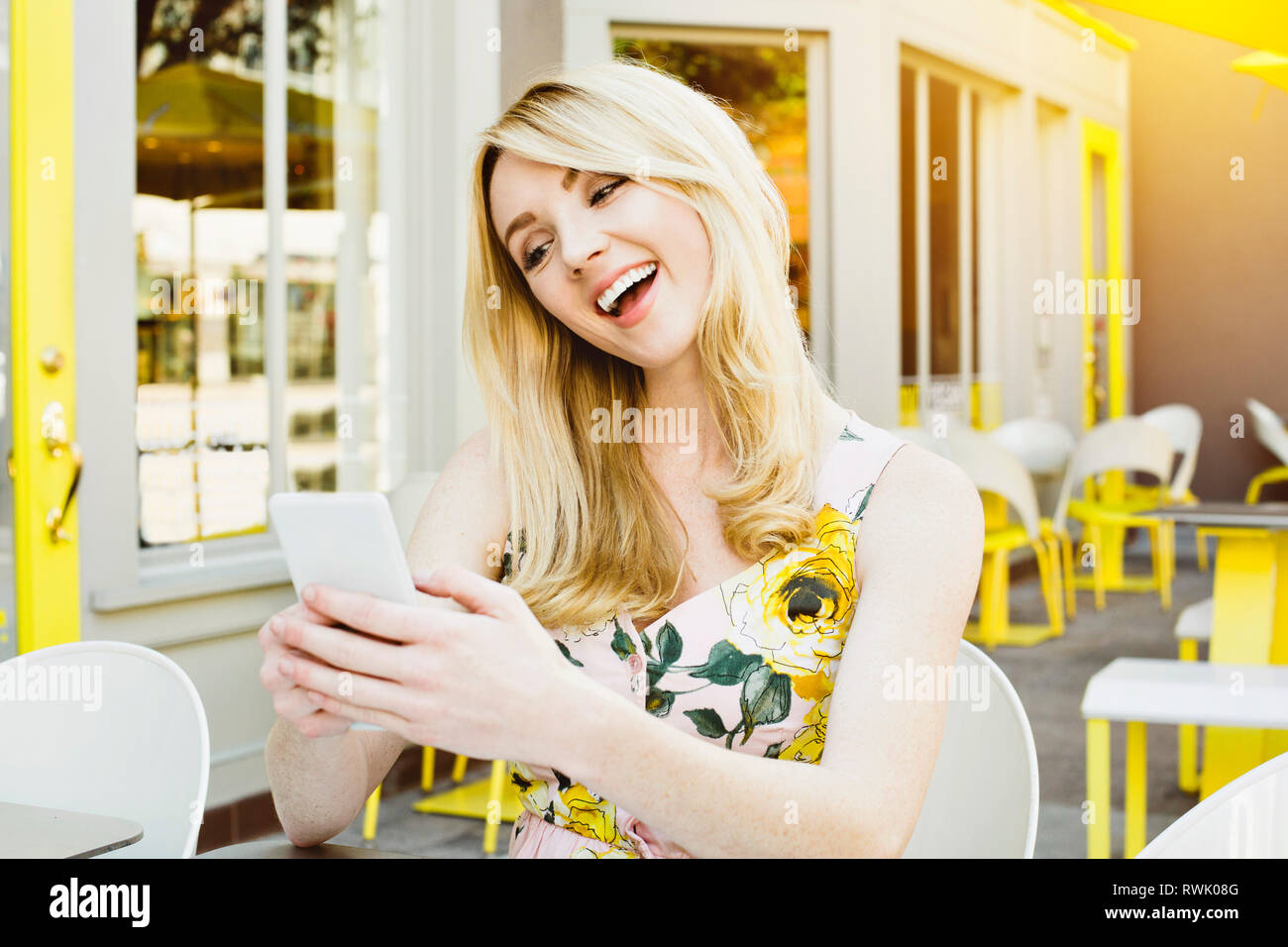 Vista frontale di una giovane ragazza bionda guardando il suo cellulare e ridere mentre all'aperto Foto Stock