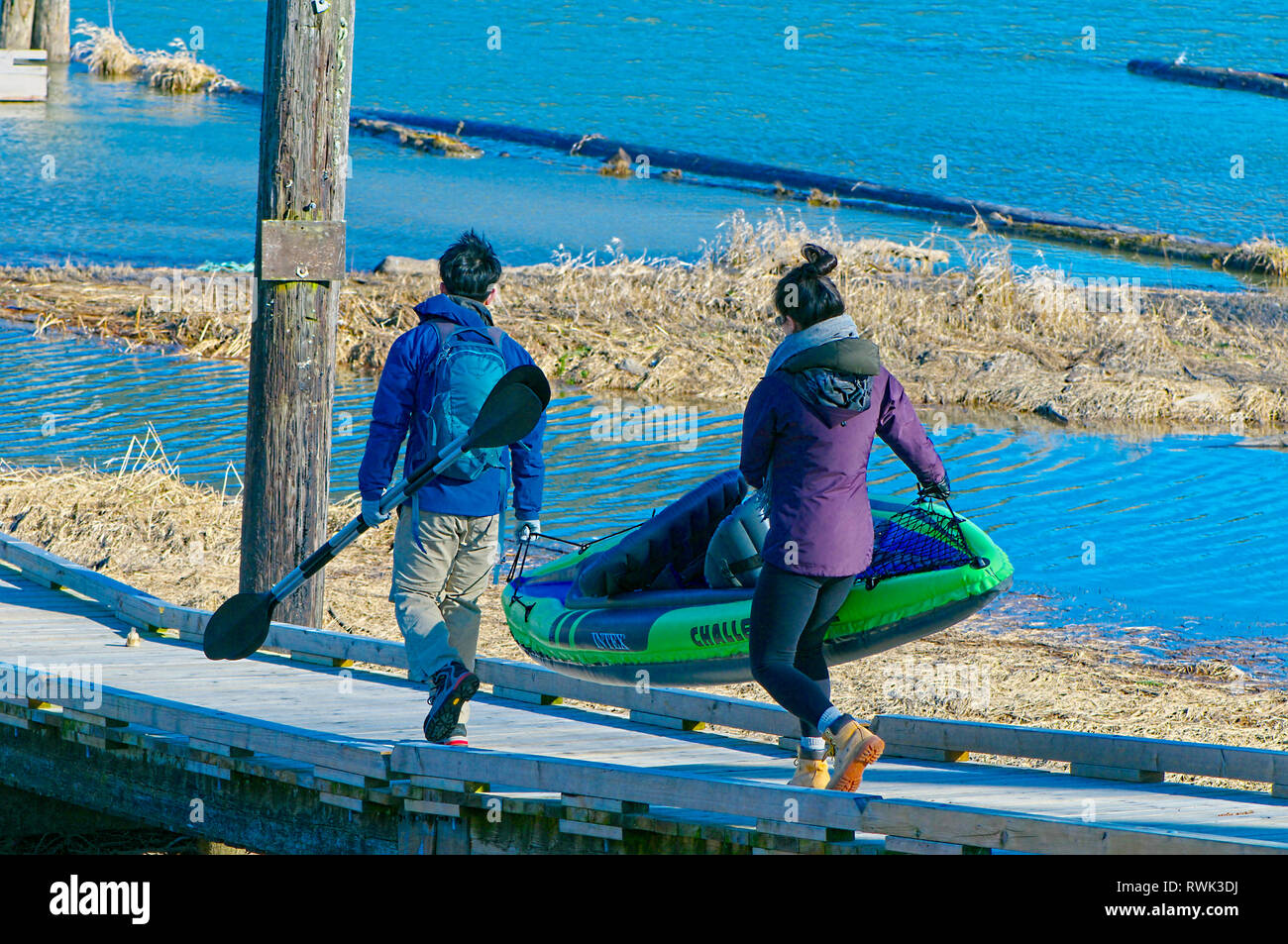 Giovani asiatici matura portante un kayak gonfiabili lungo una rampa di legno. Concessione si restringe il Parco Regionale, Pitt Prati, British Columbia, Canada Foto Stock